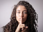 一位卷发女子手指轻触嘴唇，示意安静的特写肖像