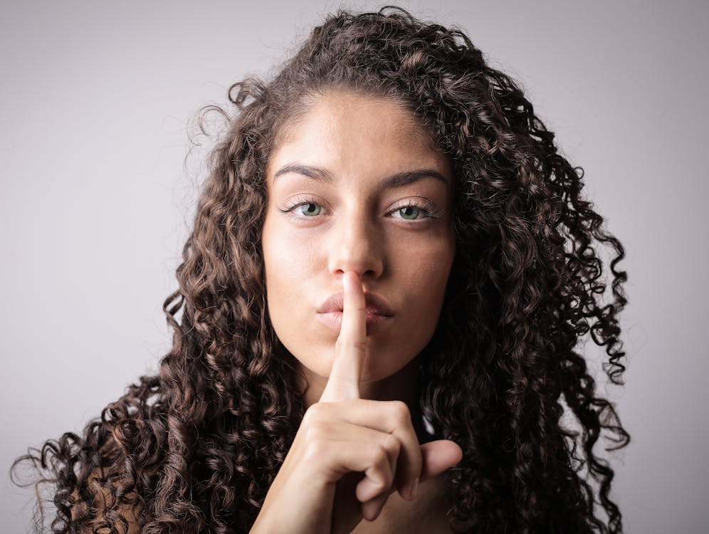 Photo of Woman with Brown Curly Hair Doing the Shhh Sign