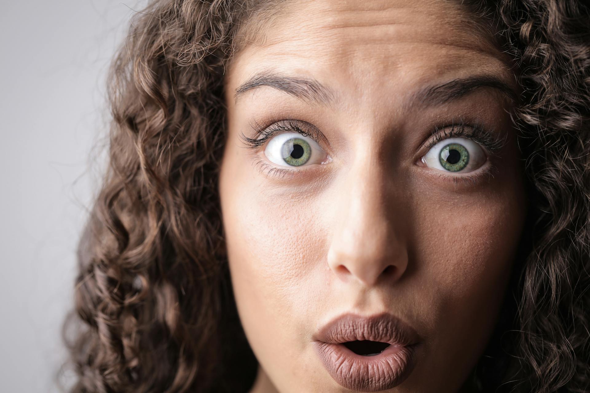 Close-up portrait of a woman with curly hair expressing surprise, highlighting her beautiful eyes and lively expression.