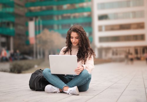 Free A woman with curly hair using a laptop while sitting outdoors, showcasing modern remote work lifestyle. Stock Photo