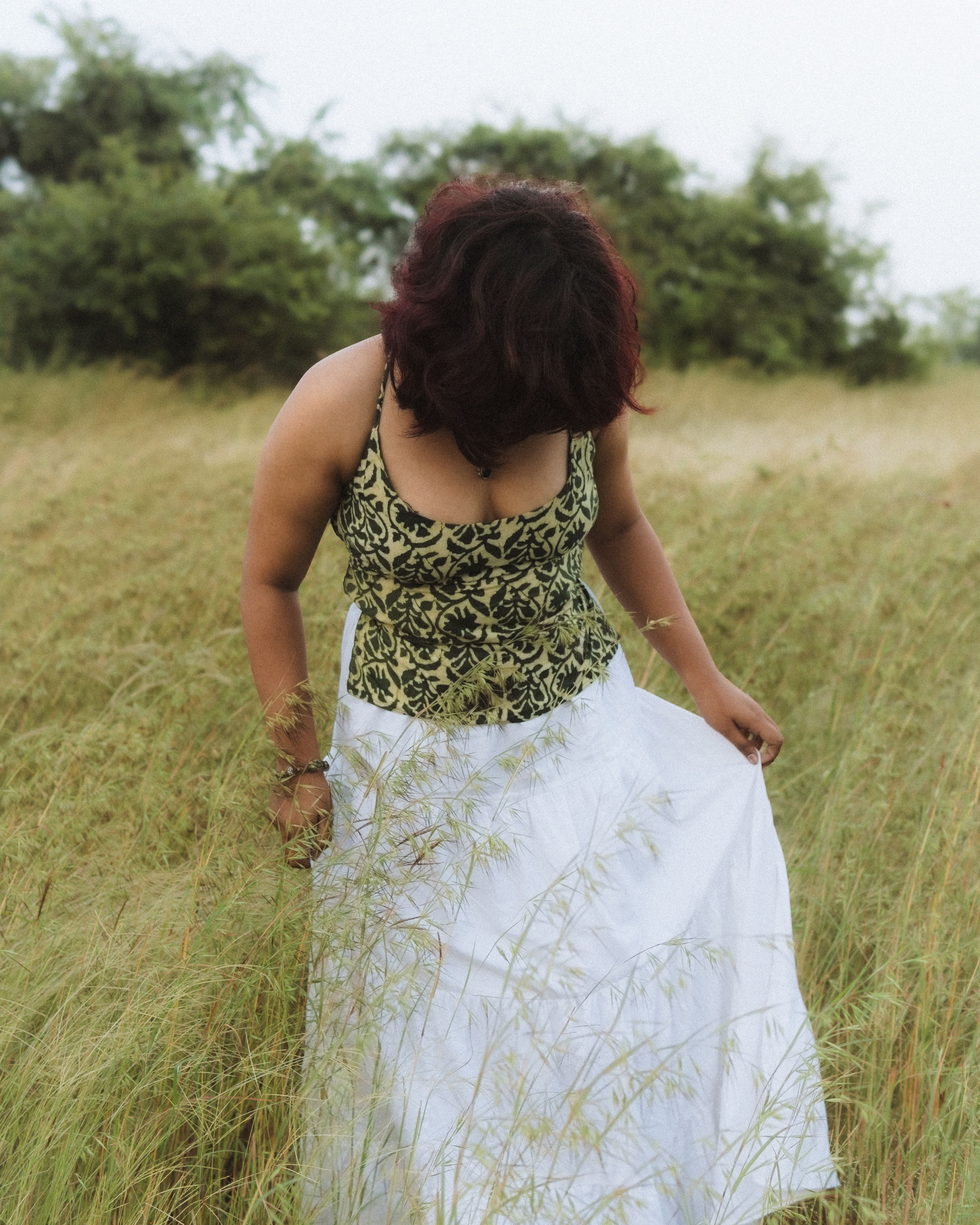 A woman wearing a floral top and white skirt in a grassy field captured during daylight.