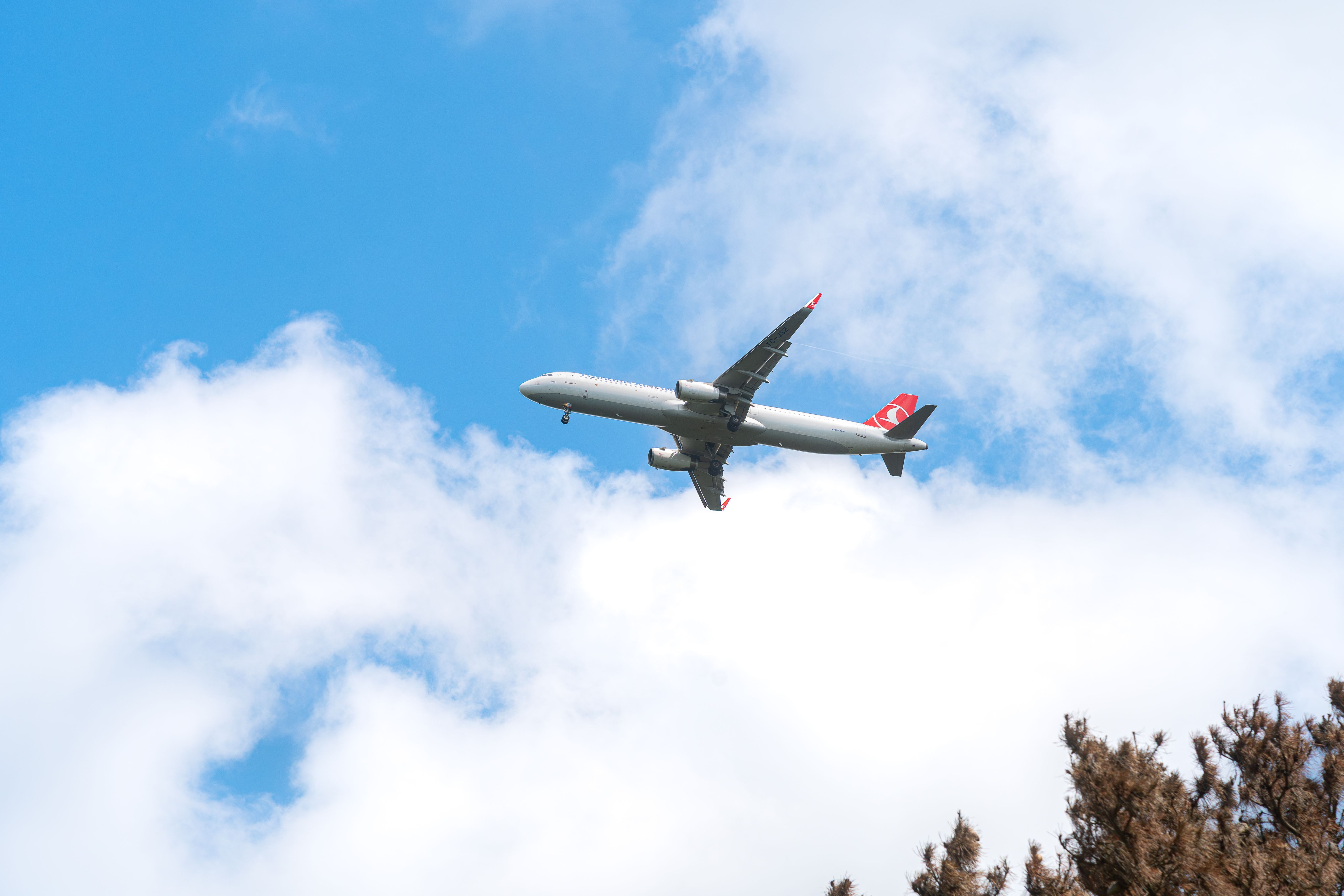 A commercial airplane flying through a clear blue sky with scattered clouds.