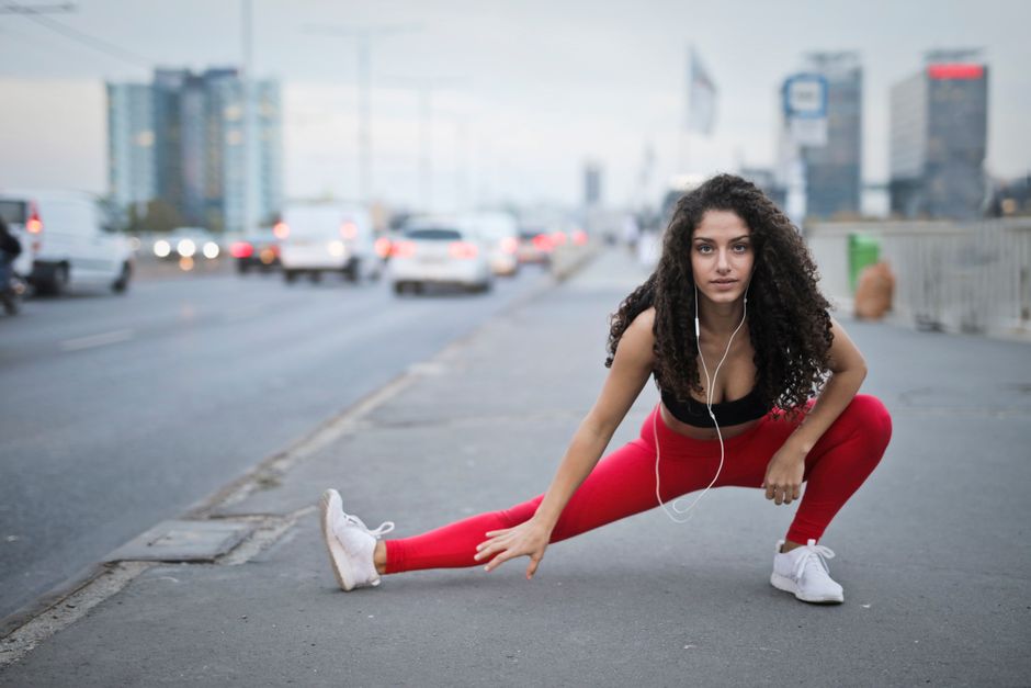 Young woman in workout attire stretching outdoors in an urban setting, exuding strength and determination.