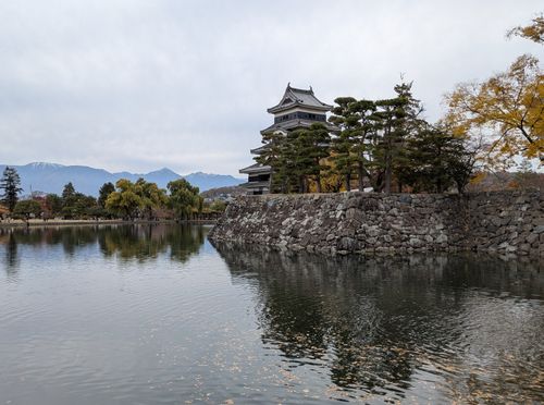 Free Matsumoto Castle reflected in a serene lake with autumn trees and distant mountains. Stock Photo