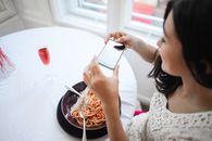年轻女子在优雅的餐厅里用手机拍摄意大利面