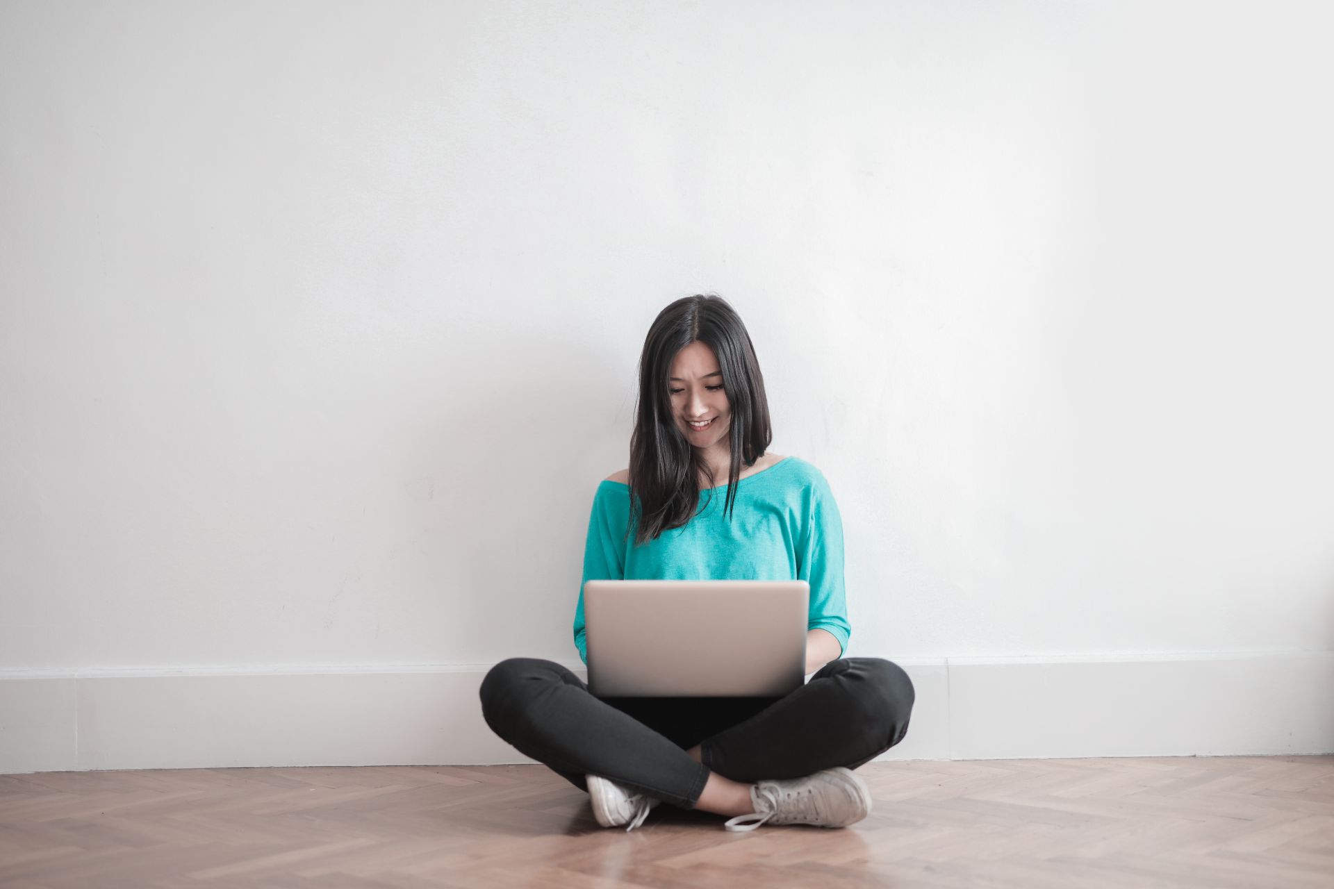 Young woman sitting indoors, smiling while using a laptop. Comfortable and casual setting.