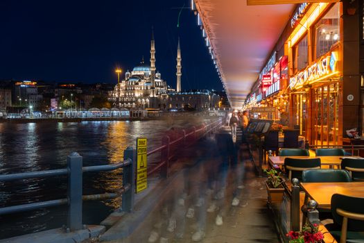 Vibrant night view of Istanbul featuring the illuminated Yeni Mosque and bustling market street.