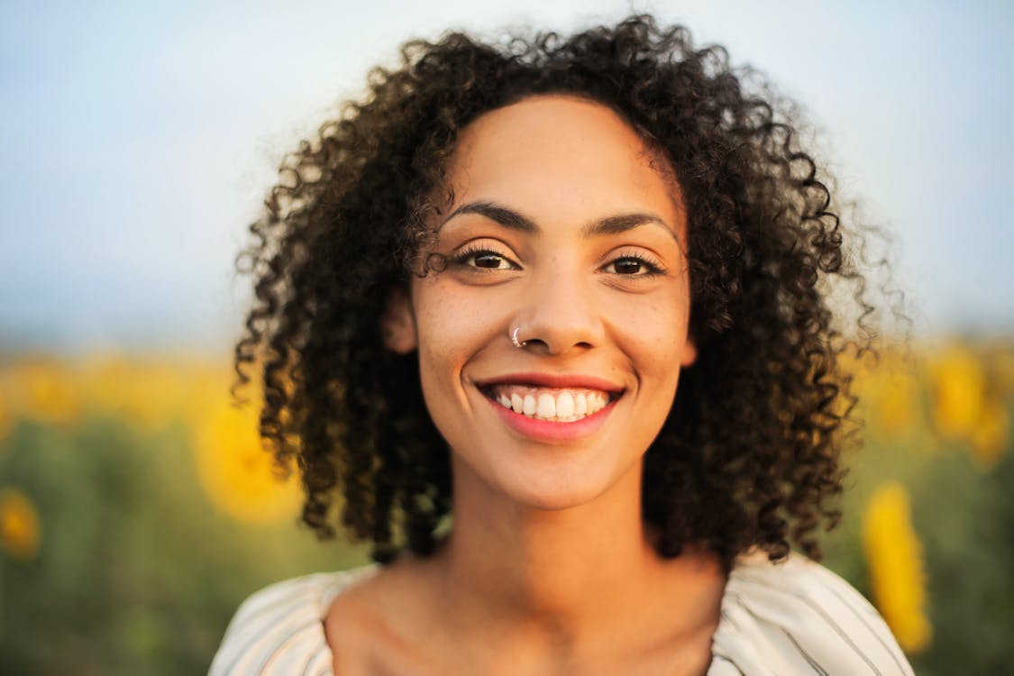 ひまわり畑の前に立っている笑顔の女性のセレクティブフォーカスポートレート写真