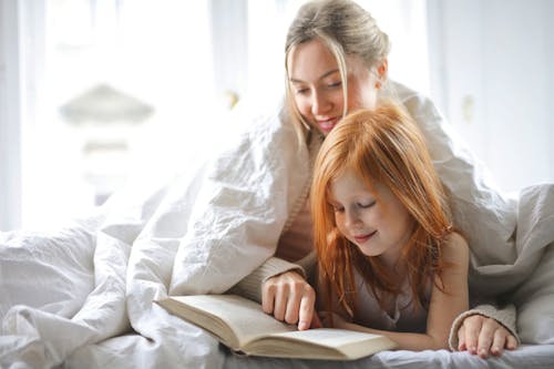 ベッドで本を読んでいる母と娘の写真