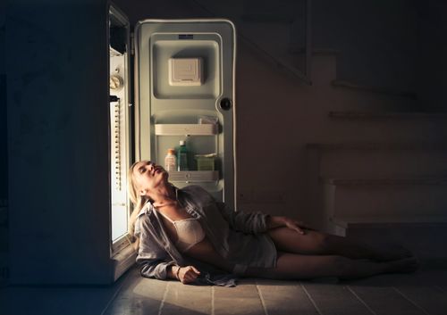 Free A woman relaxes near an open refrigerator in a dimly lit room, creating a serene and moody atmosphere. Stock Photo