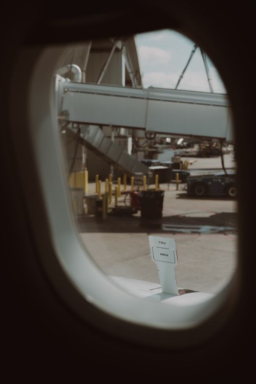 Free View of the airport tarmac and boarding gate from inside an airplane. Moody lighting and a glimpse of the wing. Stock Photo