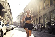 白天，一名妇女戴着耳机听音乐，在城市街道上慢跑