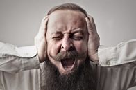Close-up Photo of Screaming Man With a Full Beard Covering His Ears and Closing His Eyes