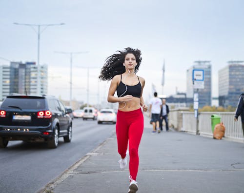 Free Photo of Woman Listening to Music on Earphones Running Down a Sidewalk Stock Photo