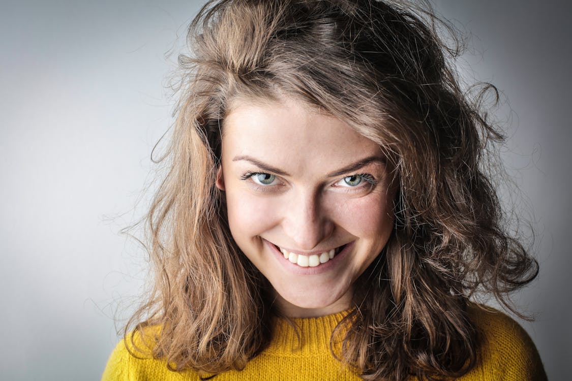 бесплатная Портретное фото улыбающейся женщины в желтом свитере Стоковое фото