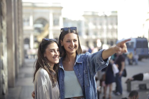 Free Happy young female friends laughing and looking away while woman in denim shirt pointing to funny place Stock Photo