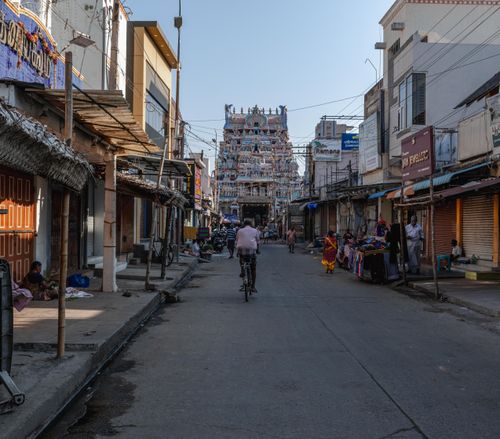 Free Bustling street with a cyclist and vendors leading to a colorful temple in Tamil Nadu, India. Stock Photo