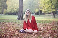 阳光明媚的公园里，一位身穿红色连衣裙的开朗女子坐在落叶中