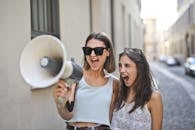 Cheerful young women screaming into loudspeaker