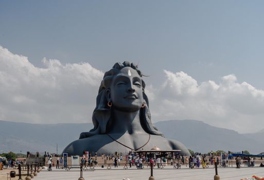 Crowd gathers at the base of the towering Adiyogi Shiva statue in Coimbatore under a blue sky.