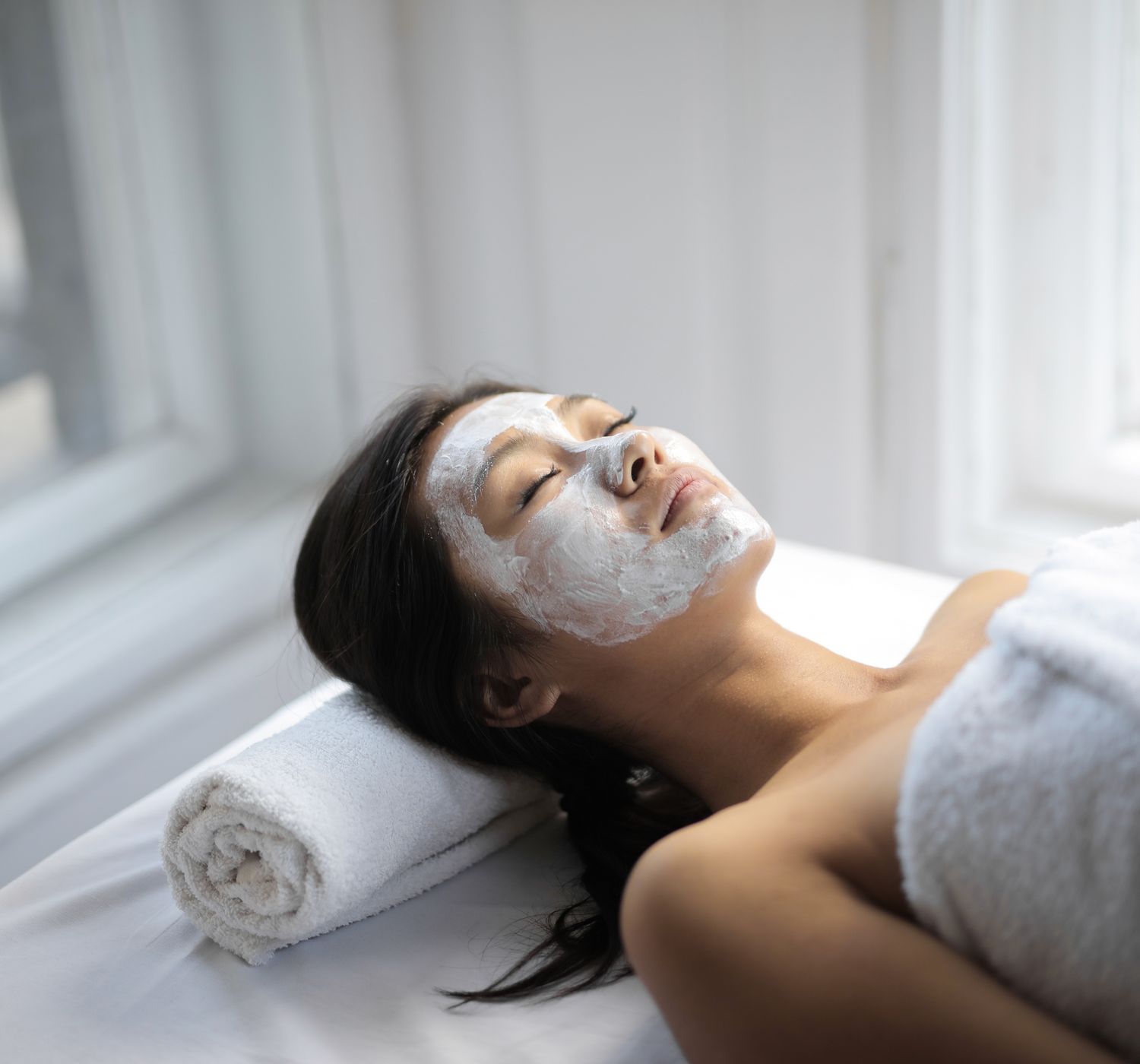 Young Asian woman on towel and with mask on face lying on covered table in light spa salon