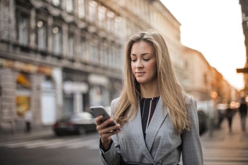 Free Businesswoman using smartphone while walking through city street, focused on phone. Stock Photo