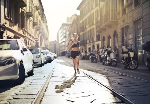 舗装された通りをジョギングしているイヤホンで音楽を聴いている女性の写真