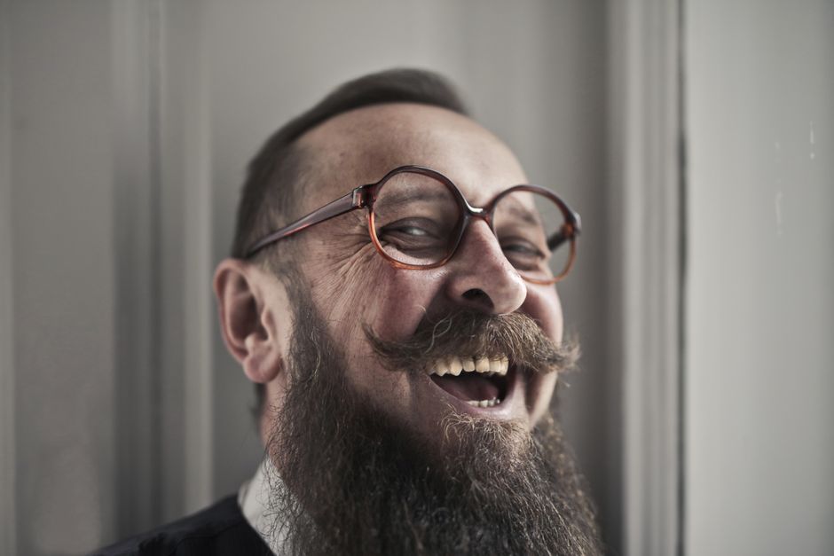 Fotomural Primer plano de un hombre barbudo y feliz con gafas riendo en interiores.