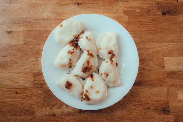 Plate of homemade Polish pierogi with crispy onions on wooden table