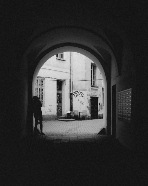 Free A silhouette stands in an archway leading to a graffiti-covered alley in Warsaw. Stock Photo