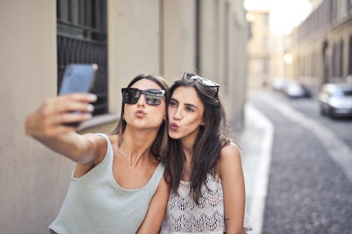 Selective Focus Photo of Two Women Standing Together Taking a Selfie
