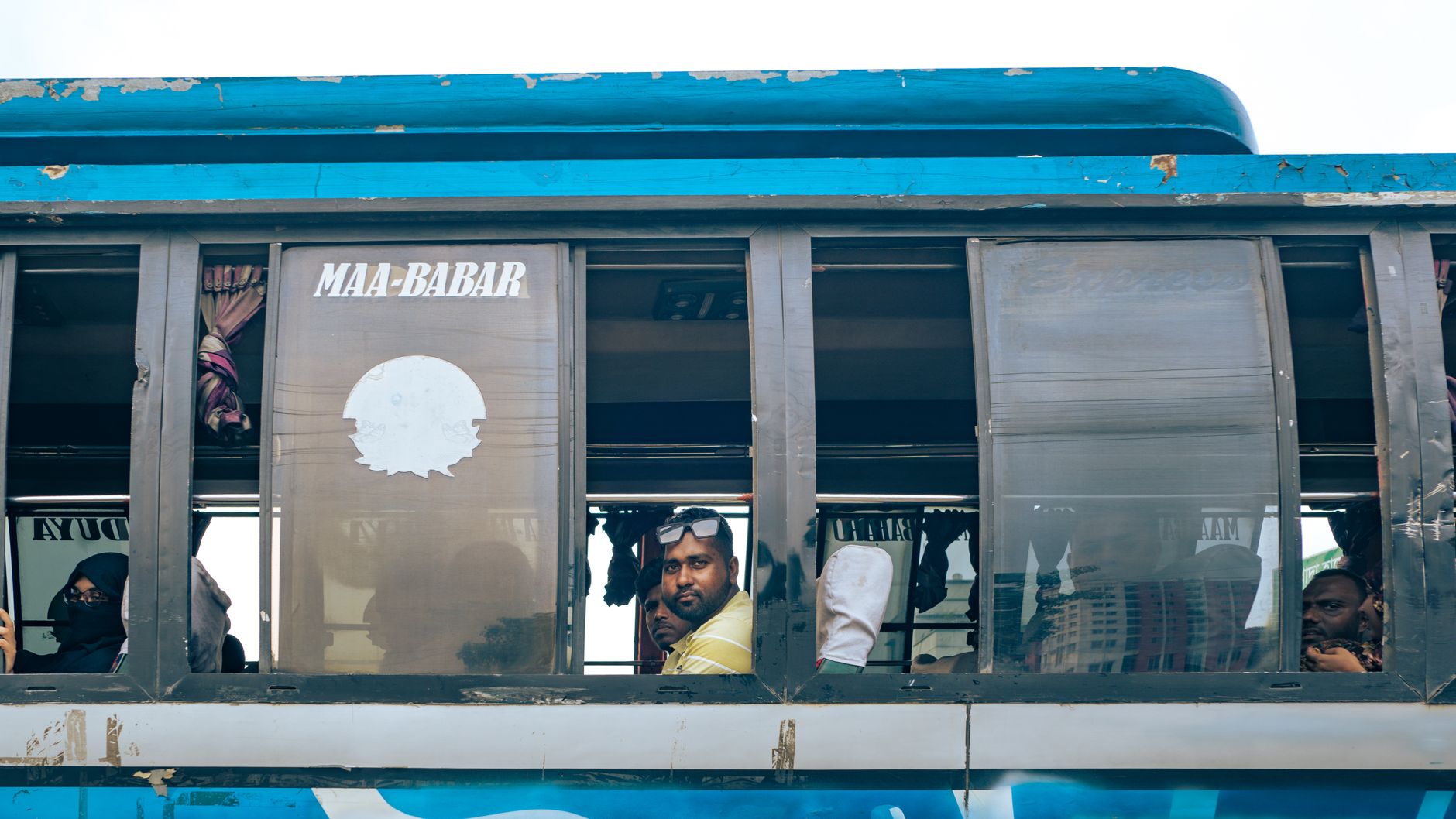 Passengers inside a vibrant blue bus in Gabtali, Rajshahi Division, Bangladesh.