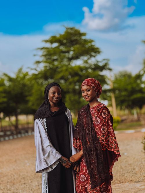Free Two women in vibrant traditional attire smiling in a sunny outdoor setting with greenery. Stock Photo