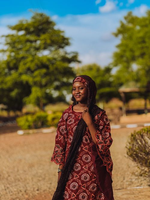 Free A woman wearing traditional African clothing smiles in an outdoor setting with trees and clear skies. Stock Photo