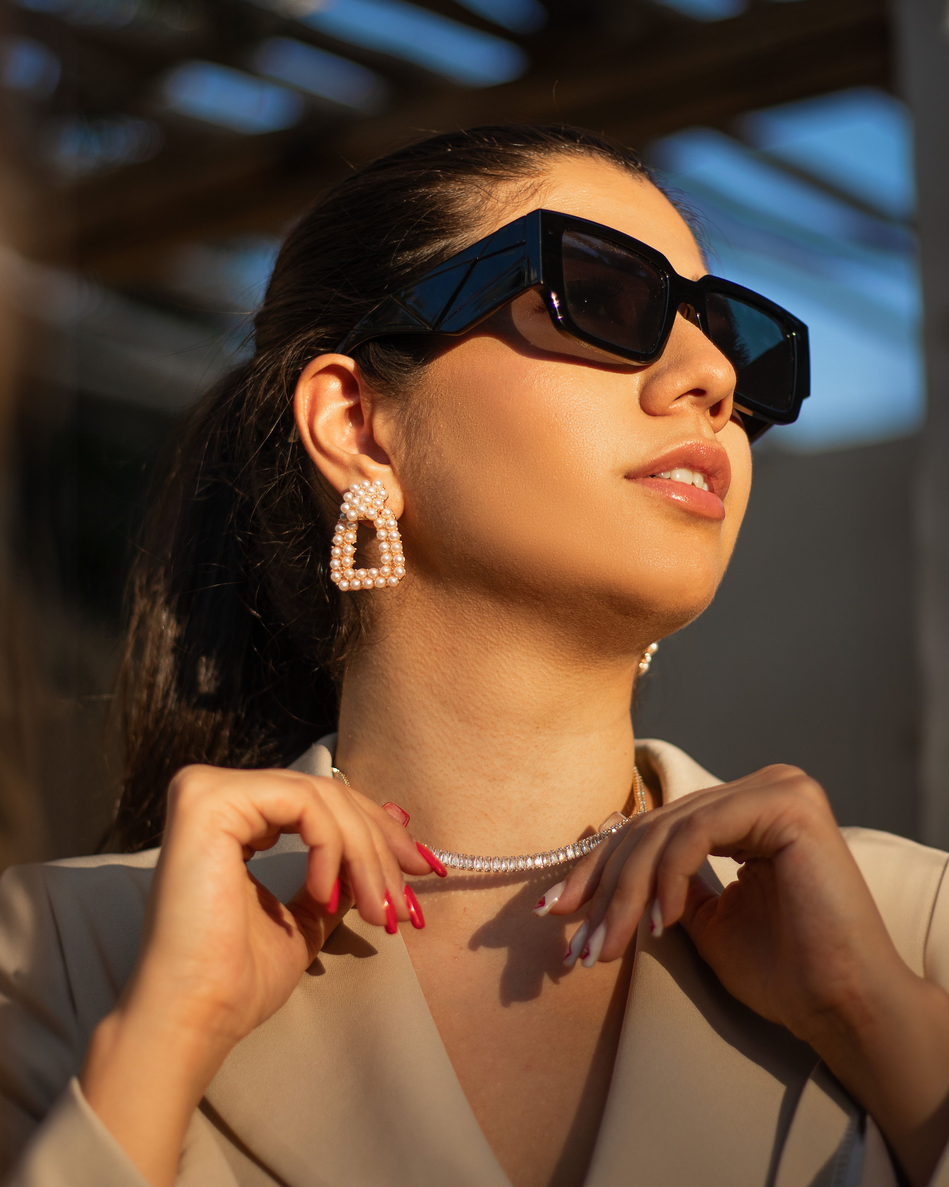 Mulher estilosa usando óculos de sol e jóias de pérola sob a luz intensa do sol, exibindo a elegância da moda.