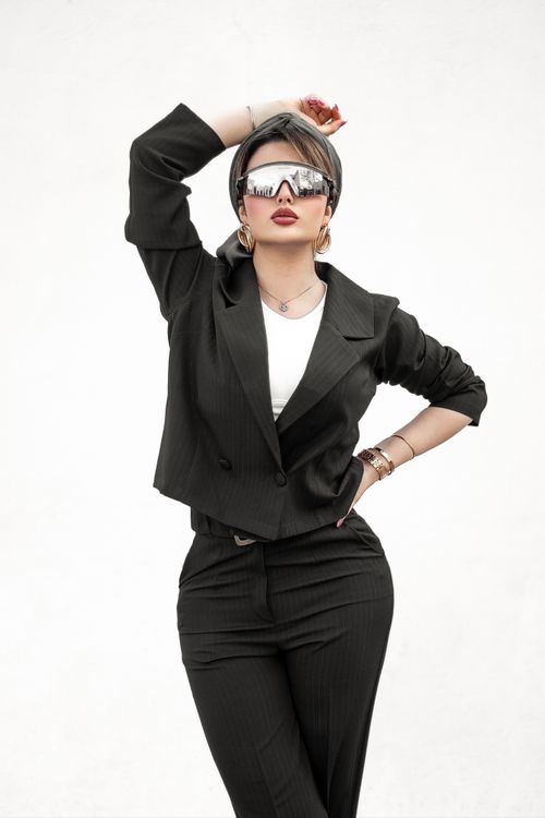 Free Confident woman in black suit with sunglasses and headscarf, striking pose. Stock Photo