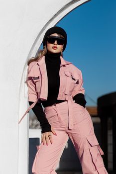 Stylish woman in pink outfit poses confidently outdoors under a blue sky.