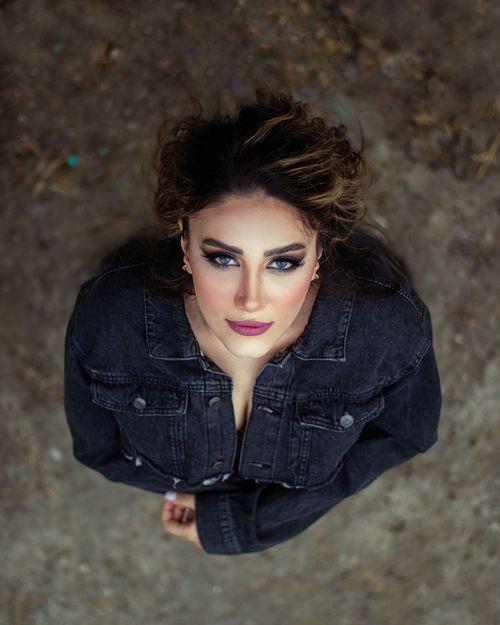 Free High-angle portrait of a woman in a denim jacket looking up with striking makeup and expression. Stock Photo