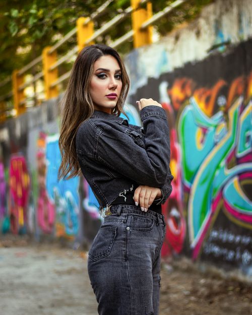 Free Stylish woman poses confidently in denim against vibrant urban graffiti wall. Stock Photo