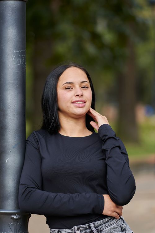 Free Casual outdoor portrait of a smiling woman standing near a pole, with a blurred nature background, in Uruguay. Stock Photo