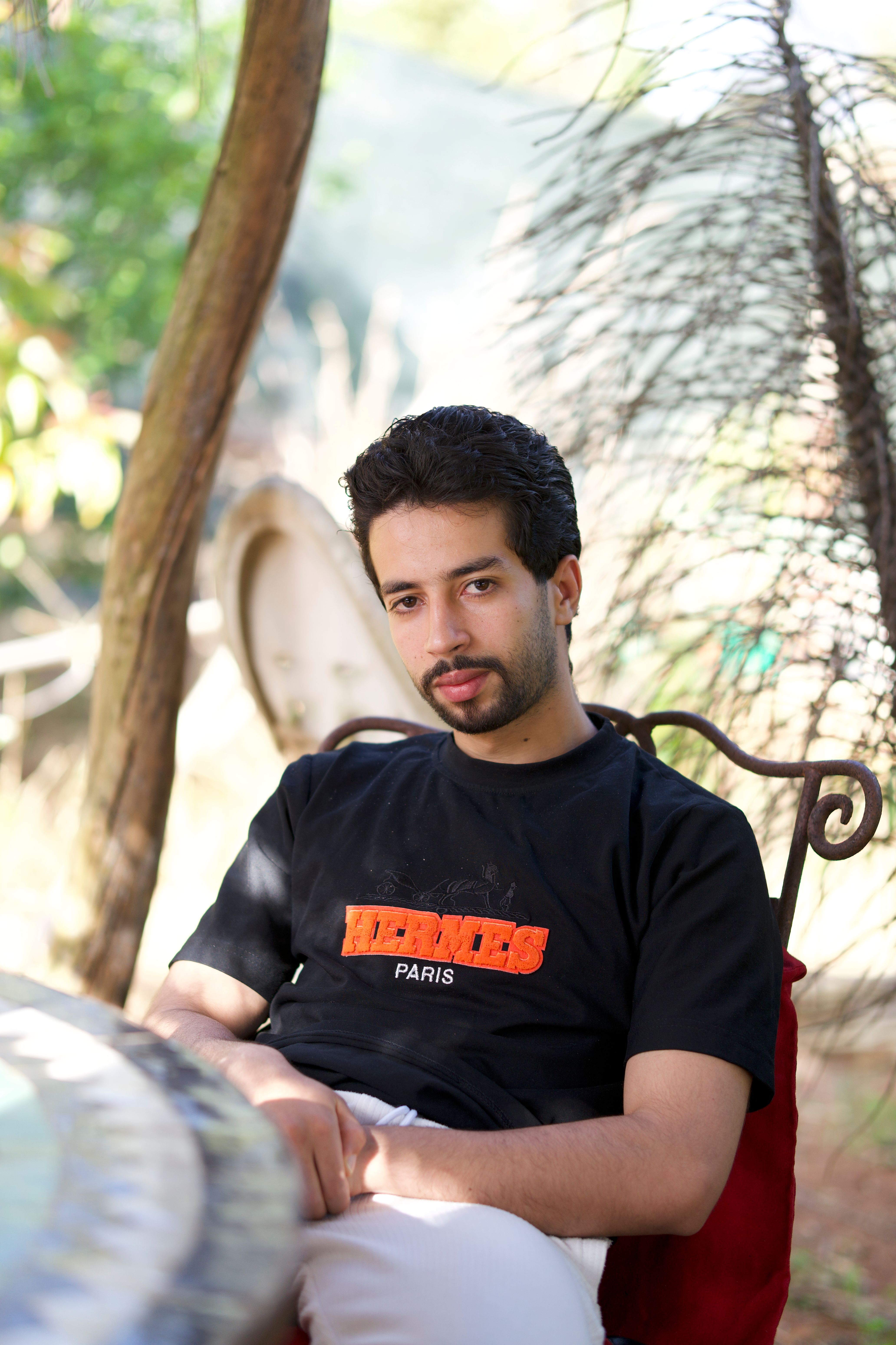 Young man sitting outdoors in a relaxed pose with natural background lighting.