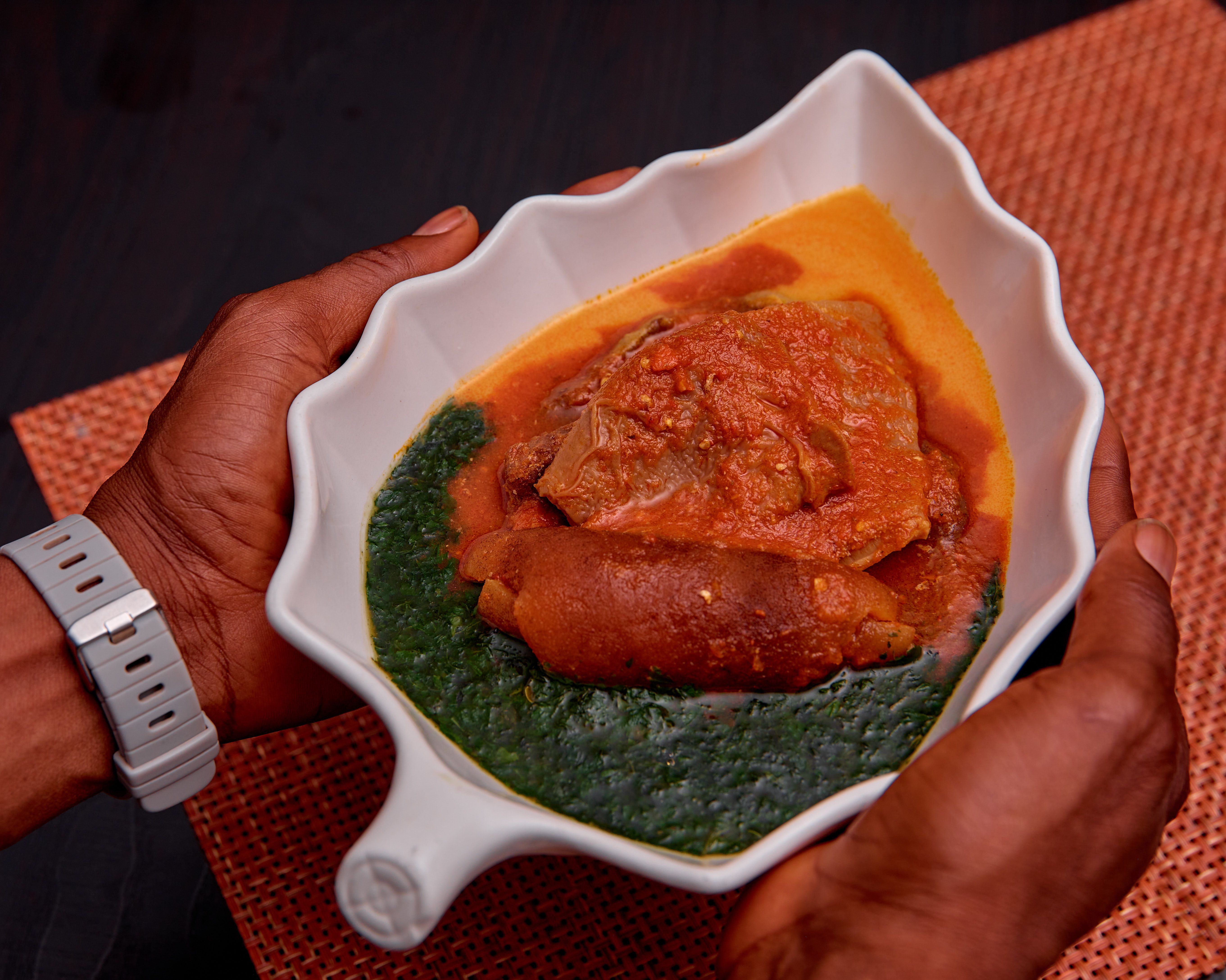 A vibrant African dish featuring meat stew and greens in a unique leaf-shaped bowl.