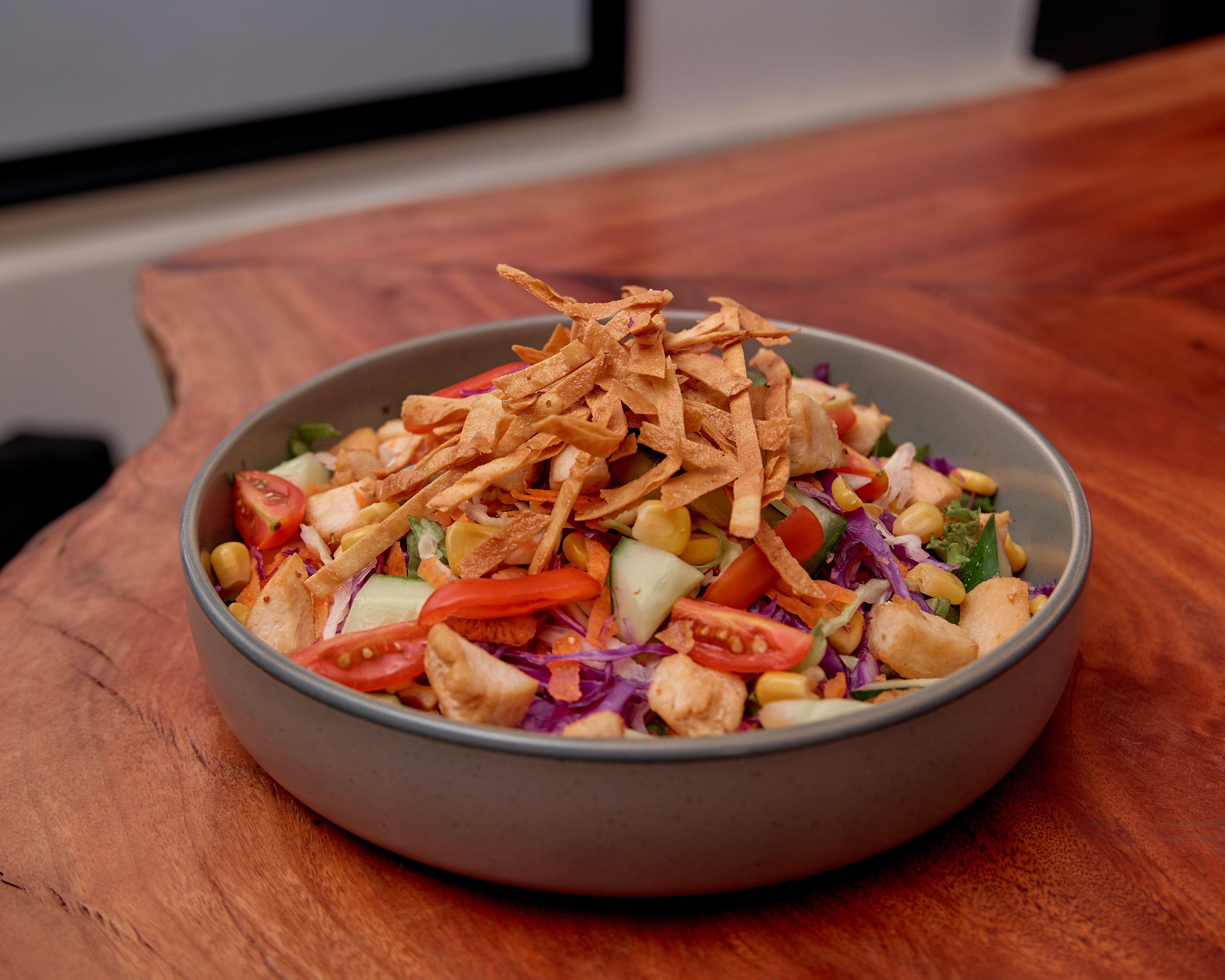 A vibrant salad with tomatoes, cucumber, corn, and tortilla strips in a bowl.