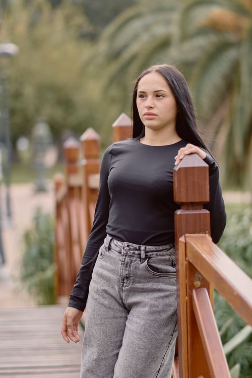 Free Portrait of a young woman leaning on a bridge, surrounded by greenery in a park setting. Stock Photo