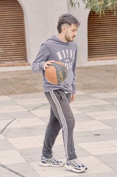 Man in casual attire dribbling a basketball on an outdoor court, captured in a relaxed setting.