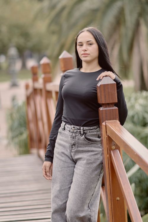 Free A young woman stands confidently on a wooden bridge in a lush, outdoor setting, exuding natural beauty. Stock Photo