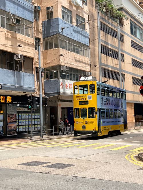 Free A classic yellow double-decker tram navigates the bustling streets of Hong Kong, capturing urban life. Stock Photo
