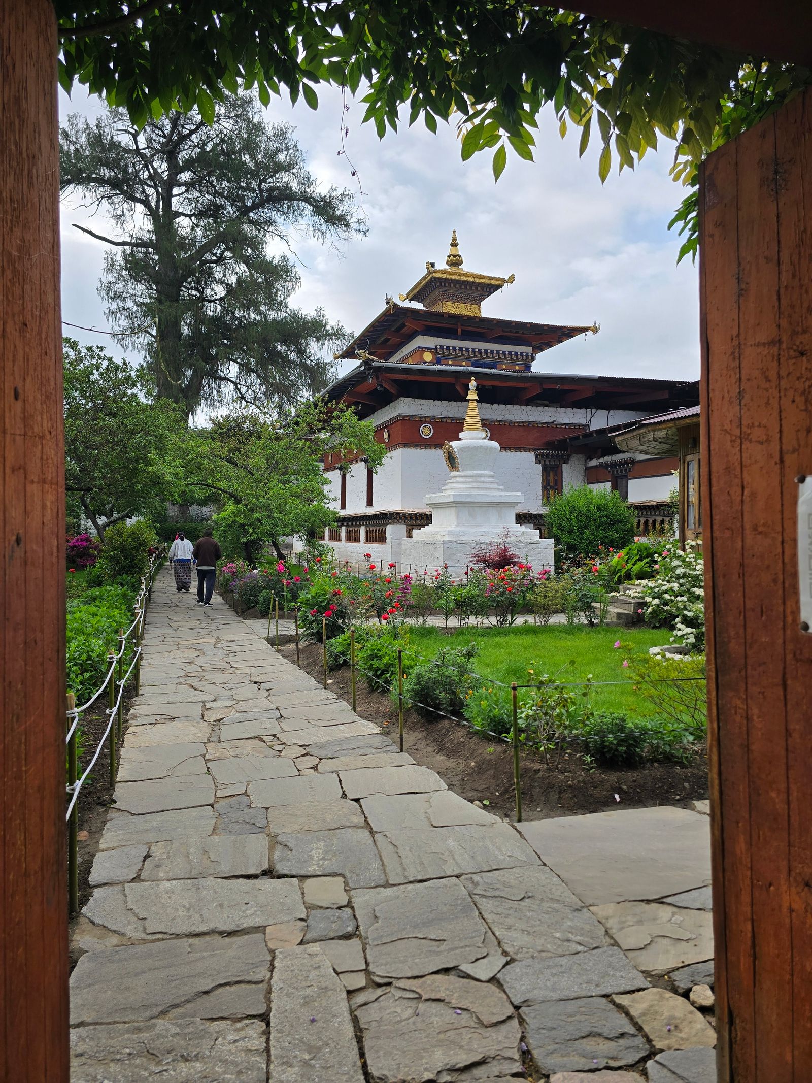 Stone path through the rose garden of Kyichu Lhakhang to its white chorten and gold roofed temple, framed by the gate