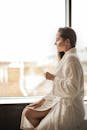 一位穿着浴袍的宁静女子手持香槟酒杯，凝视着窗外