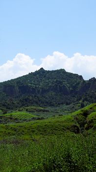 Scenic view of verdant hills against a bright blue sky with fluffy clouds.